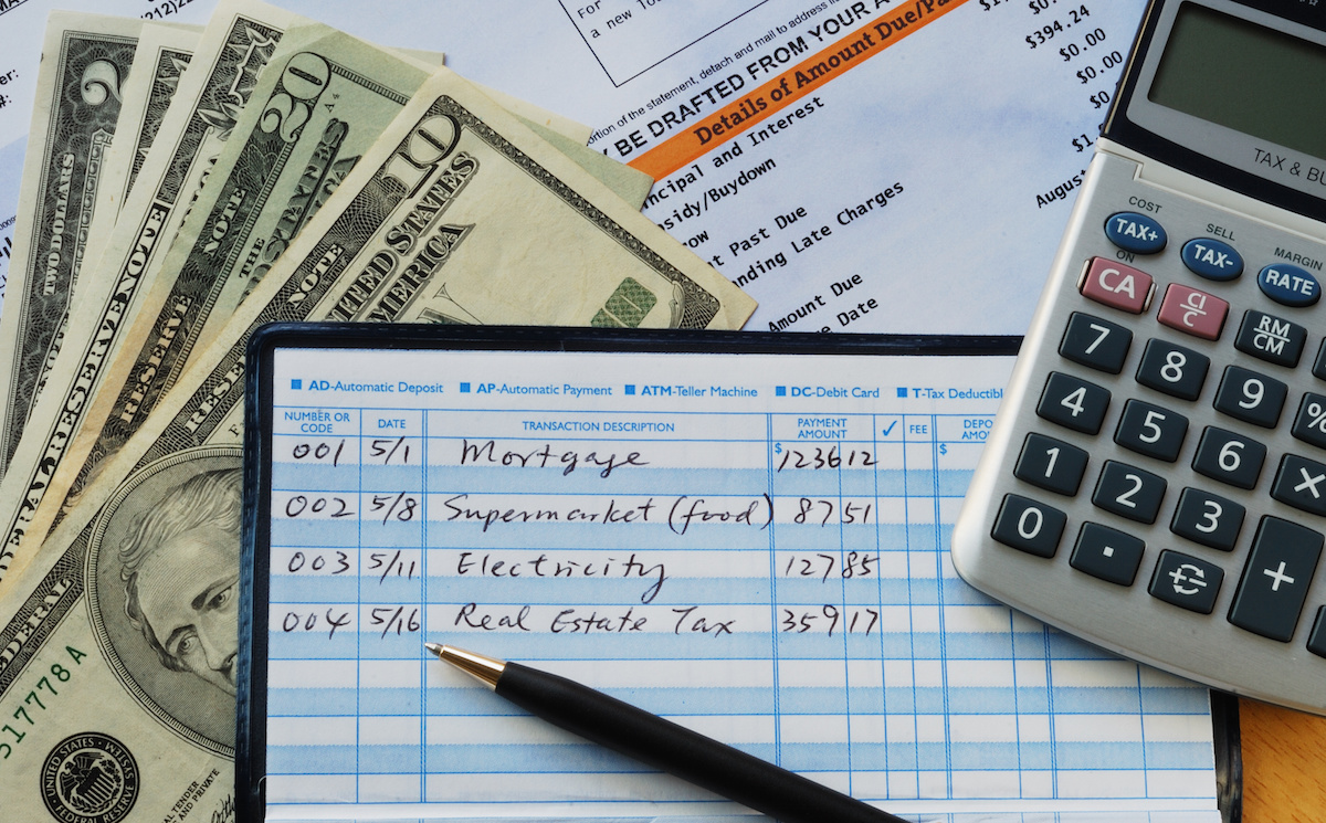 A check register, calculator and cash laid out for monthly bill paying